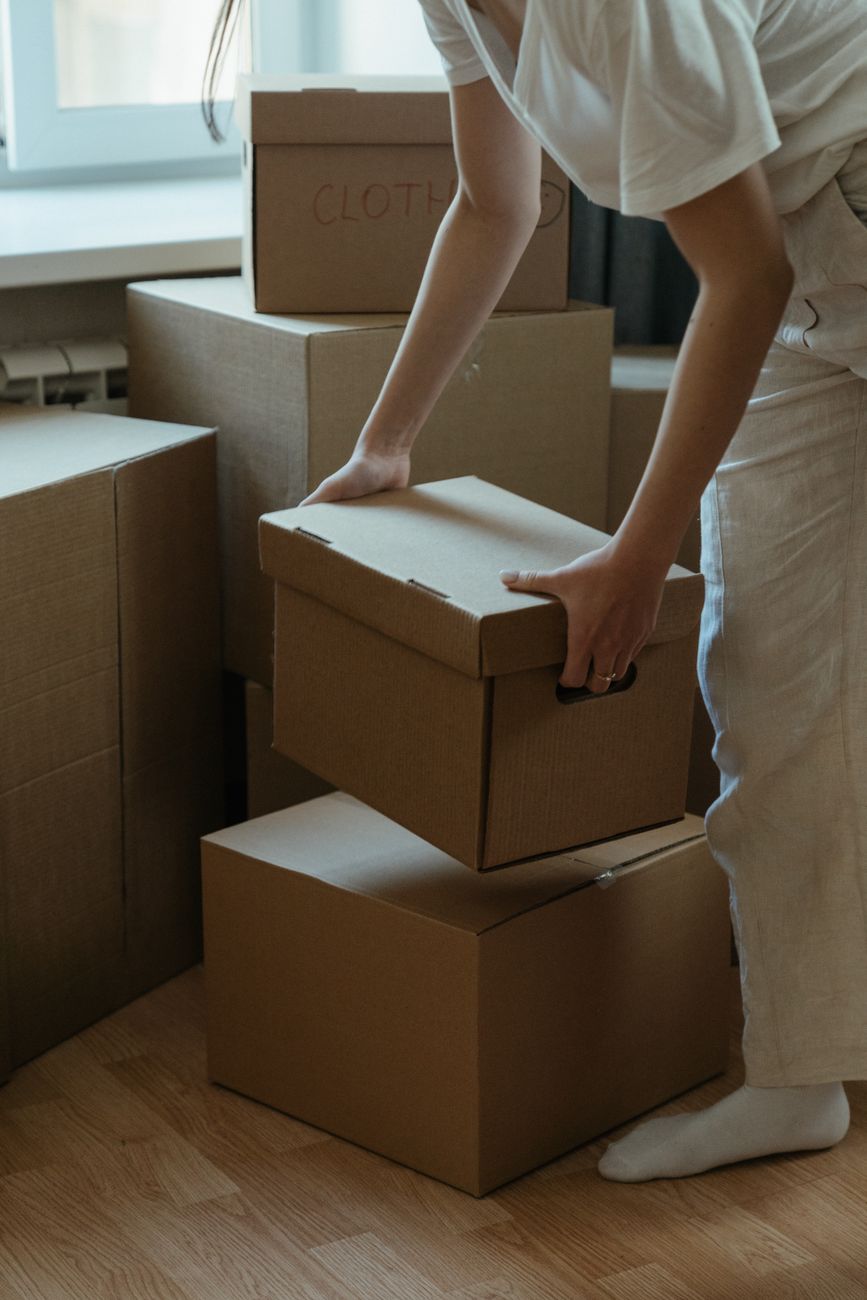 person in white pants holding brown cardboard box